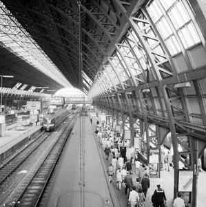 881972 Gezicht op de perrons onder de eerste perronkap van het N.S.-station Amsterdam C.S. te Amsterdam.